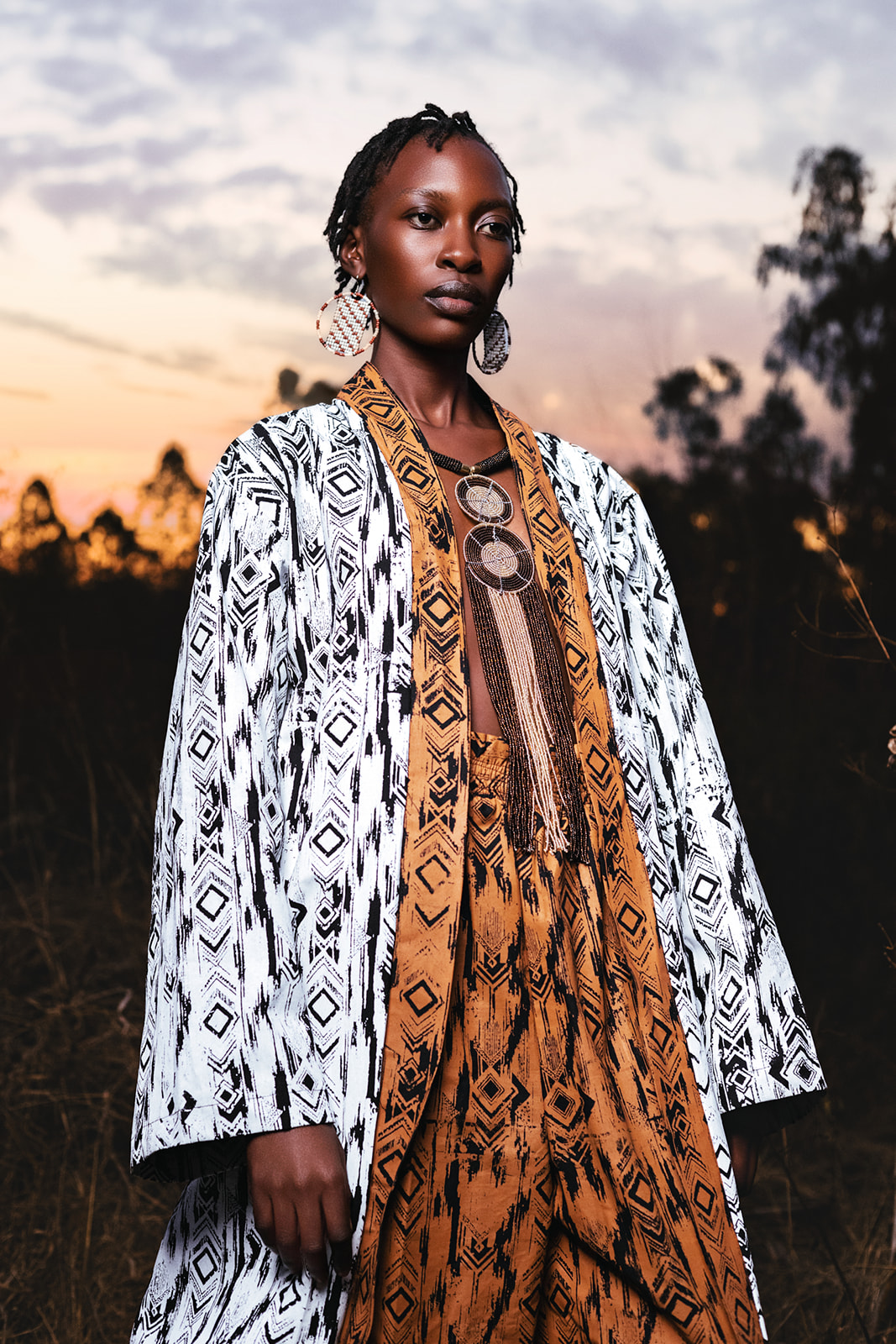 Model in ochre MOSI print bucket hat and white geometric scarf, confident pose at dusk.